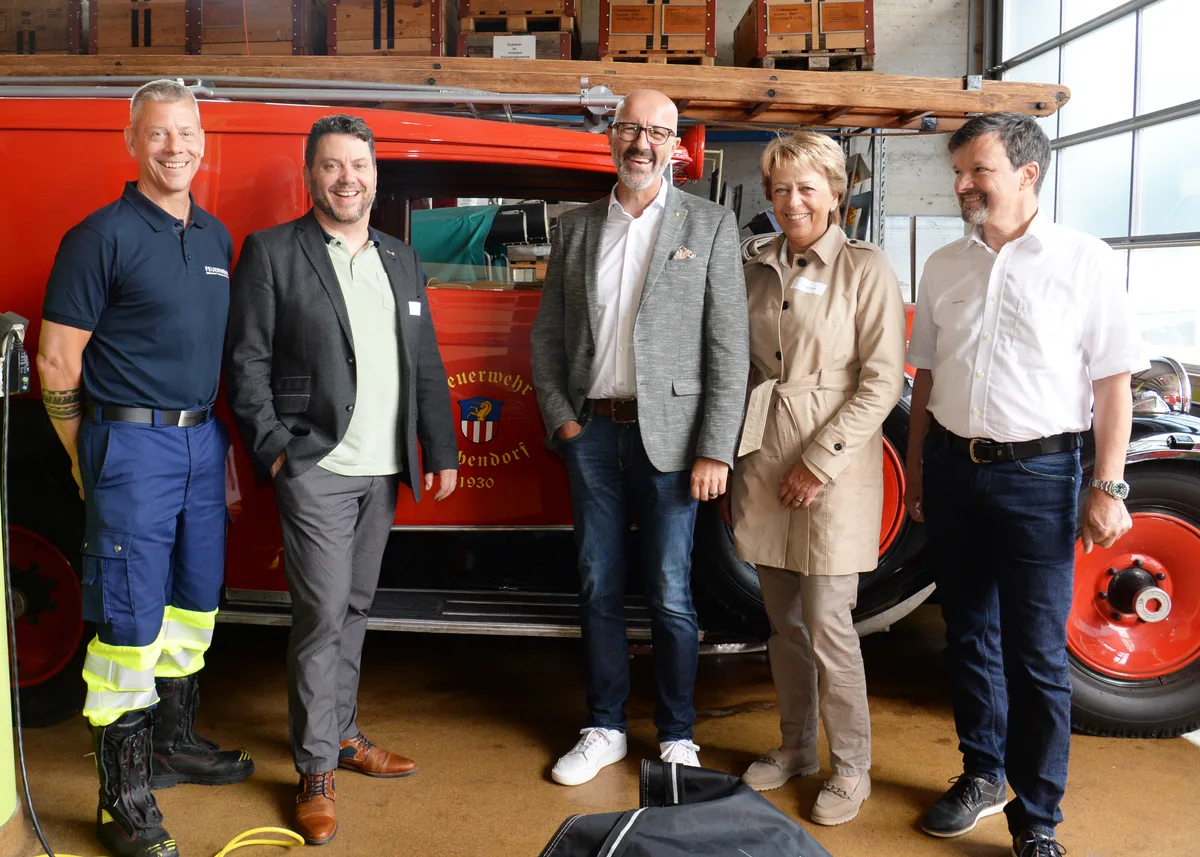 Mehrere Personen posieren vor einem alten Feuerwehrauto. 